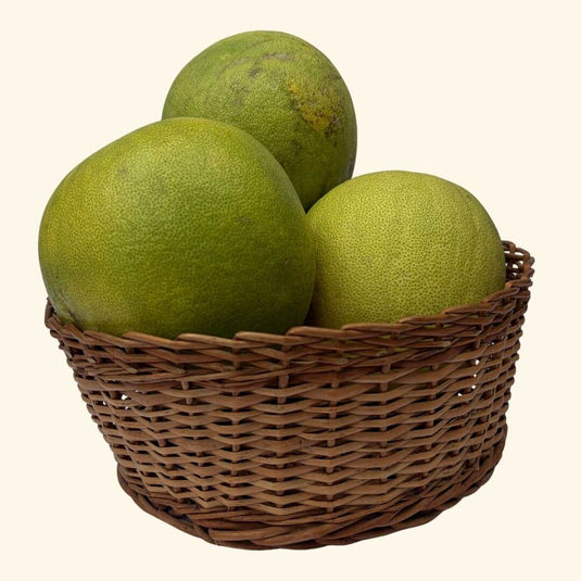 The Staple Kaka green pomelos in a woven basket on a white background